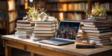 a laptop on a table with books and a vase of flowers