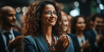 a person with curly hair wearing glasses and a suit and holding her hands together